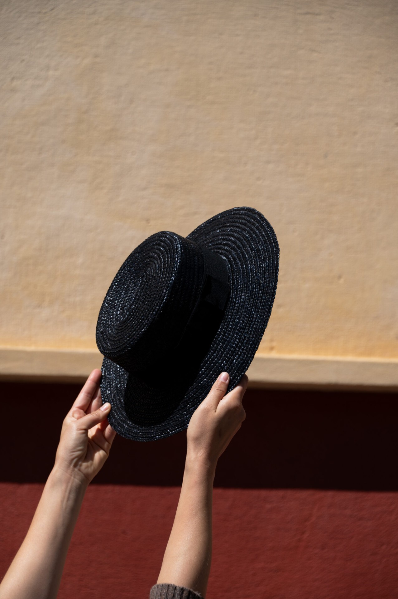 Cappello di paglia nero sollevato contro un muro ocra